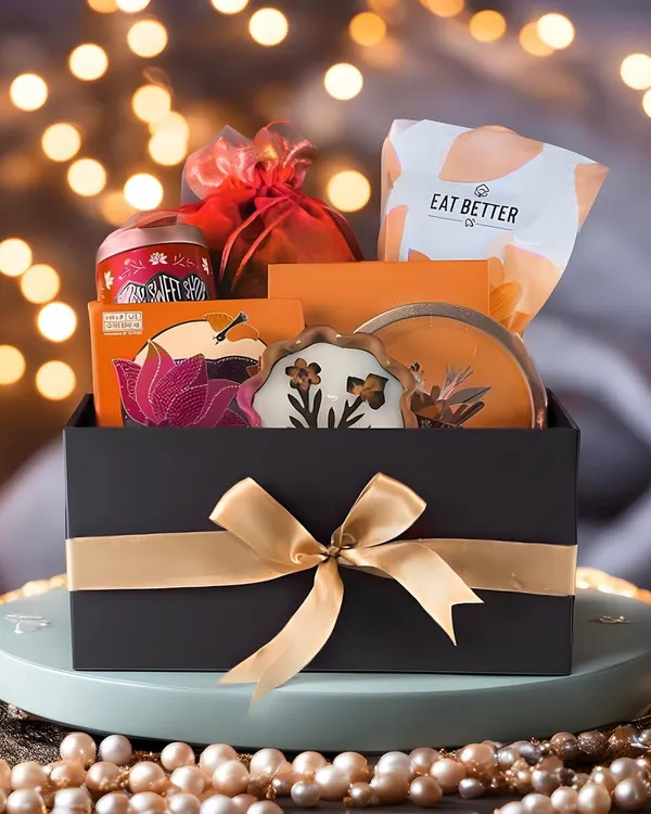 Hero Item: This is what we mean by thoughtful luxury. A beautifully curated hamper in our signature black box, tied with a gold ribbon and set against a warm, festive glow, perfect for making any occasion feel special.