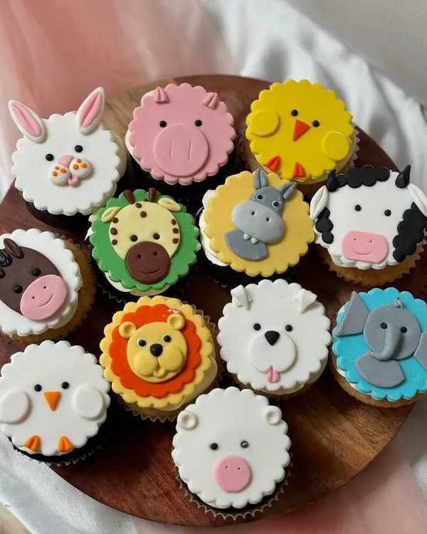 A dozen cupcakes featuring a variety of handcrafted fondant animal faces. This set includes a lion, elephant, pig, sheep, dog, horse, cow, hippo, giraffe, bunny, chick, and pig, showcasing the detailed 2D fondant work I can create for animal-themed parties.