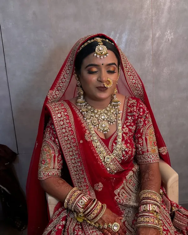 A moment of quiet elegance before the ceremony begins. This North Indian bride looks serene with her classic red lehenga, intricate jewelry, and perfectly blended HD makeup.