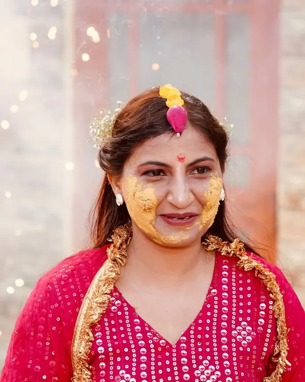 A candid shot of a woman during a Haldi ceremony, with her face covered in turmeric paste. The sparklers in the background add a festive and celebratory feel to this joyful moment.