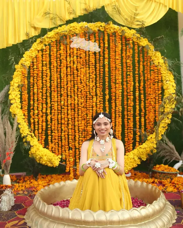 A happy bride at her Haldi ceremony, seated in front of a magnificent circular backdrop made entirely of fresh marigold strings. I added a neon 'Haldi' sign for a modern touch.