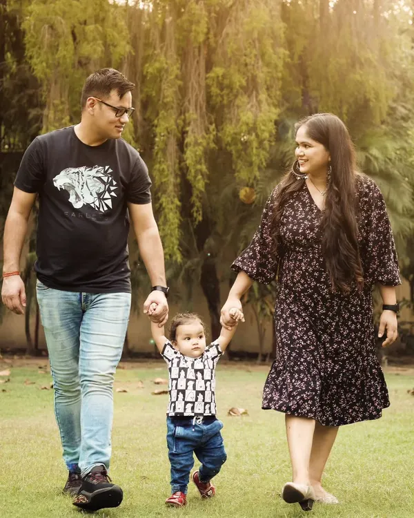 A beautiful family portrait taken outdoors, with parents holding their child's hands as he takes his first steps.