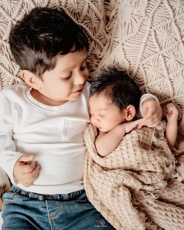 The beginning of a lifelong friendship. A big brother gently holds his sleeping newborn sibling in this heartwarming and tender portrait.