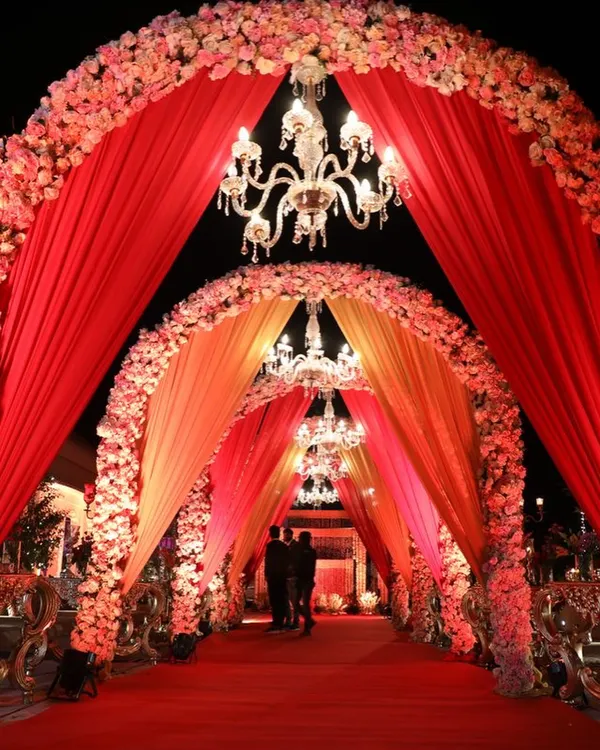 A truly royal entrance with cascading red and orange floral arches and crystal chandeliers. This grand walkway is designed to make a statement.
