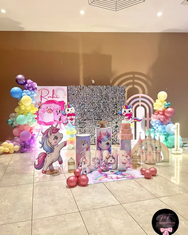 The main stage for Ruhi's unicorn-themed first birthday. This setup features a silver sequin backdrop, pastel balloon garlands, a unicorn castle, and multiple custom props.