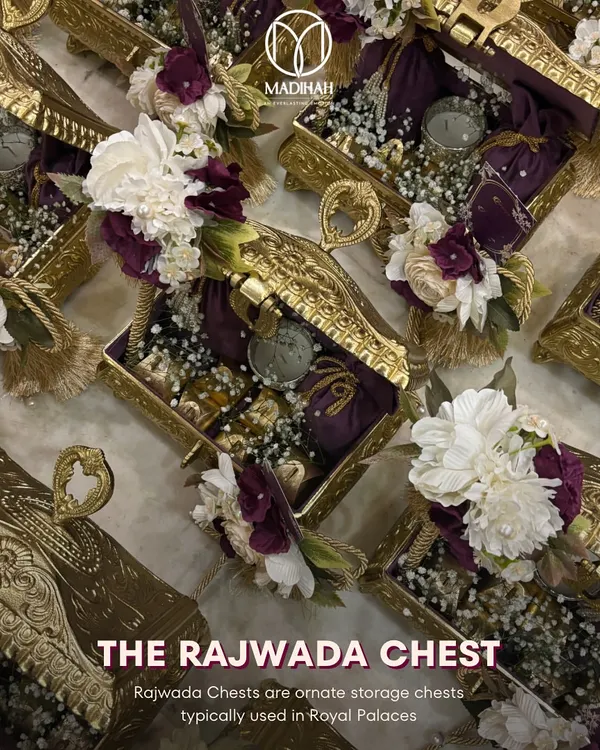 The Rajwada Chest is the epitome of royal gifting, perfect for a wedding. This overhead view showcases the intricate gold-finished metalwork and the rich floral arrangements that adorn these ornate keepsake boxes, ready to be filled with bespoke treasures.