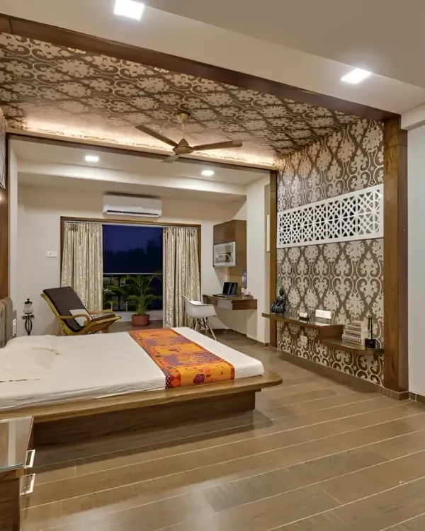 This spacious master bedroom features intricate jaali work on the ceiling and as a partition, adding a touch of traditional elegance. The low wooden bed and integrated study nook create a cohesive and luxurious space.