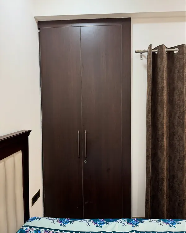 A dark wood finish wardrobe from a 2BHK apartment project in Noida Extension.