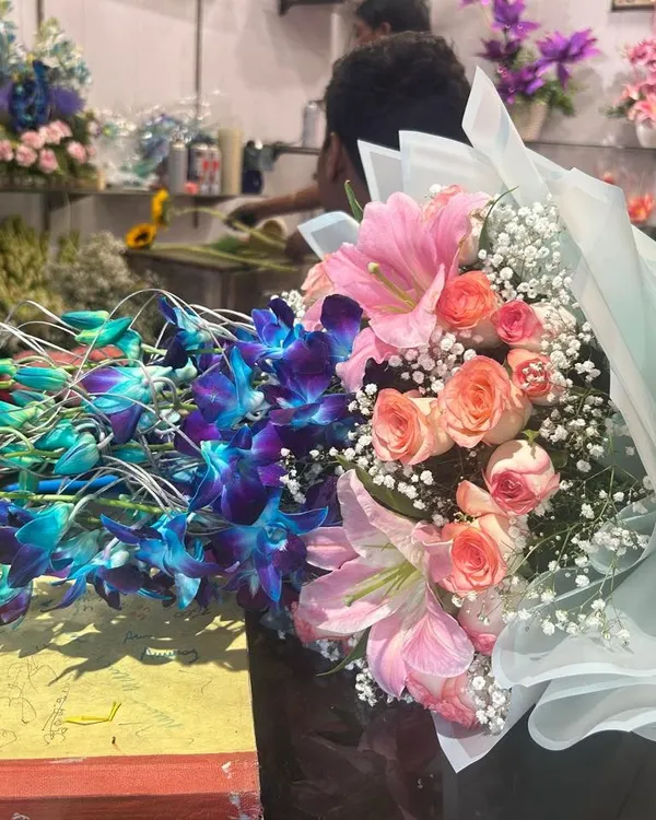 This bouquet of blue orchids, pink lilies, and roses is being prepared in my shop. You can see the freshness and care that goes into every order.
