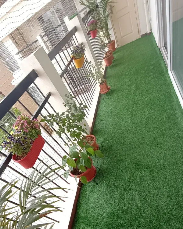 A long apartment balcony is instantly upgraded with a full carpet of artificial grass. It provides a soft surface underfoot and complements the potted plants along the railing.