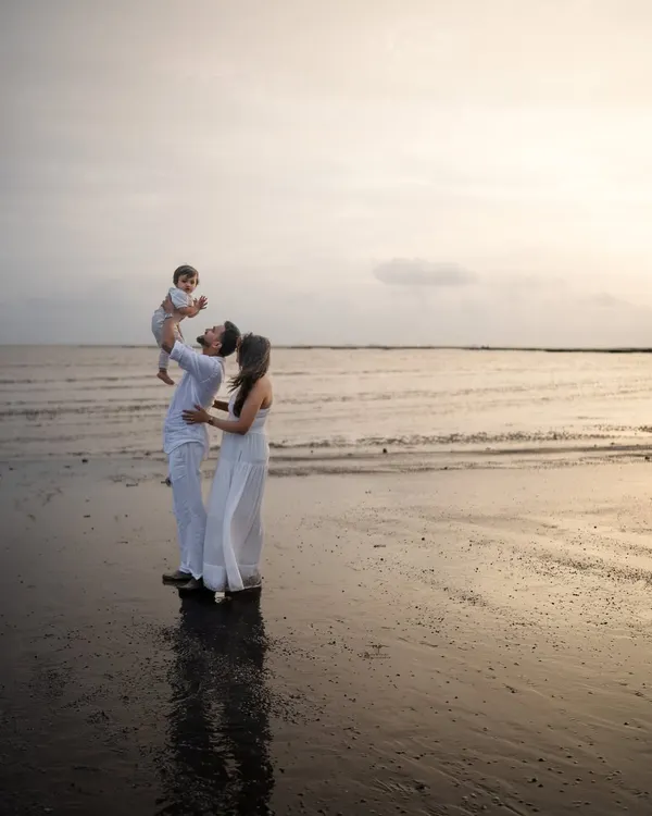 A father lifts his child towards the sky as the sun sets over the ocean. This silhouette-style shot captures a classic, heartwarming moment during a beach family photoshoot.