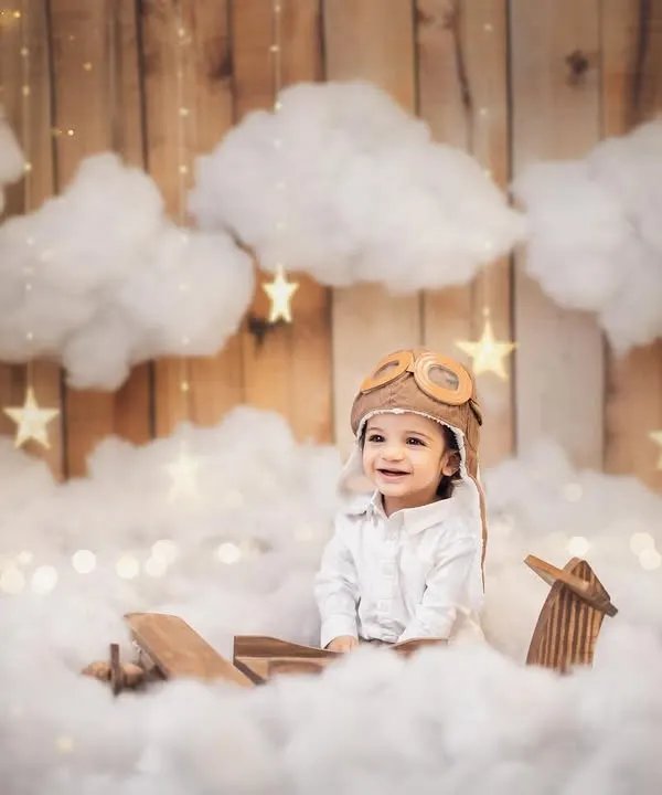 Our little pilot is ready for his first birthday adventure. Dressed in an aviator cap, this baby boy's smile lights up the whimsical cloud-filled set. This is a perfect example of a themed baby boy photoshoot.