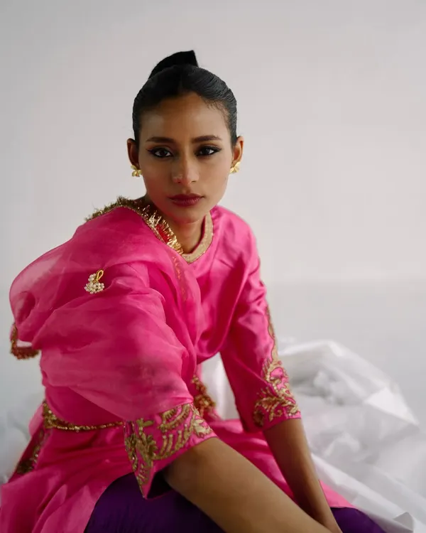 A vibrant portrait for designer Esha Arora. The bright pink of the kurta stands out against the clean white background, with a direct gaze creating an engaging image.