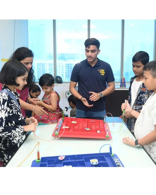 An instructor explains the rules of the steady-hand maze to a group of eager children and parents. This game tests focus and fine motor skills and is a hit with all ages.