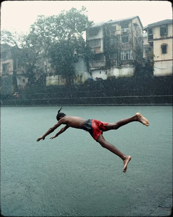 A boy captured mid-flight as he dives into the historic Banganga Tank during a downpour. This is a classic, joyful Mumbai monsoon moment.
