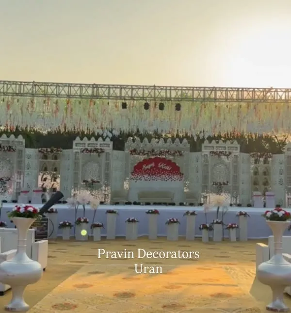 This is what I love to do: transform a vast open ground into a royal palace for your big day. This grand wedding stage, set against the sunset, features intricate white paneling, a personalized monogram, and a massive truss setup overhead, showing the scale of our work.