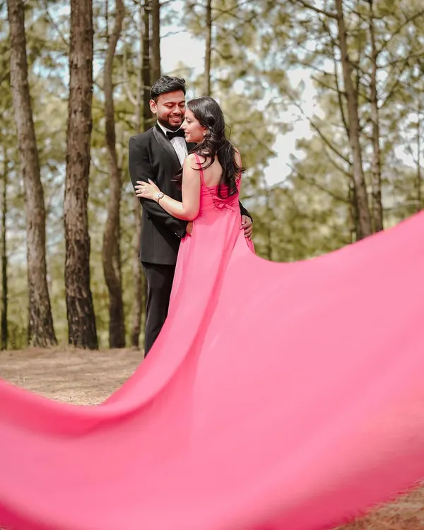 A dramatic and romantic pre-wedding portrait, using the flow of the gown's long train to create a sense of movement and artistry against the natural backdrop of the woods.