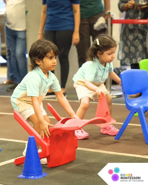Giggles, races, and playful wins. Two children navigate an obstacle course with chairs, learning coordination and problem-solving during our fun-filled Sports Day.