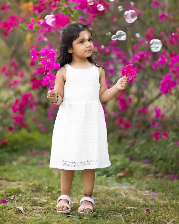 A little girl in a white dress stands in front of vibrant pink bougainvillea, with bubbles floating around her. Outdoor sessions allow for such magical, spontaneous moments.