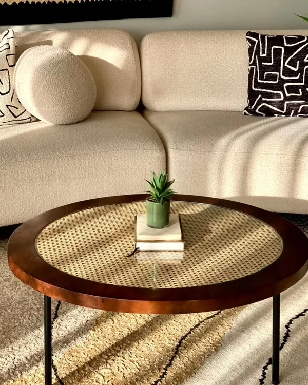 A beautiful round centre table with a dark wood frame and a natural cane weave top, protected by glass. This piece adds warmth and texture to a modern living room.