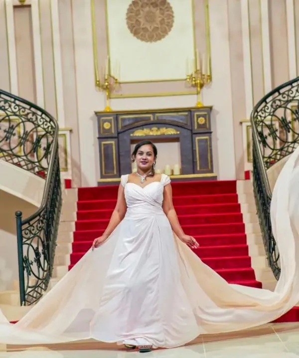 Make a grand entrance with our white trail gown. The extra long, flowing fabric adds a dramatic touch to this shot on a red carpet staircase.