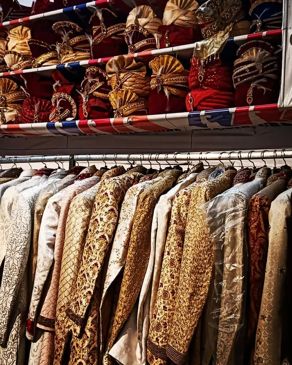 My store is packed with options. Here you can see racks filled with sherwanis in various fabrics and designs, with a full shelf of pagris and safas right above.