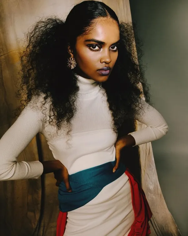 A powerful studio portrait from the 'ANAINA' series, with the model looking directly at the camera. The voluminous hair, bold makeup, and simple styling create a confident and captivating image.
