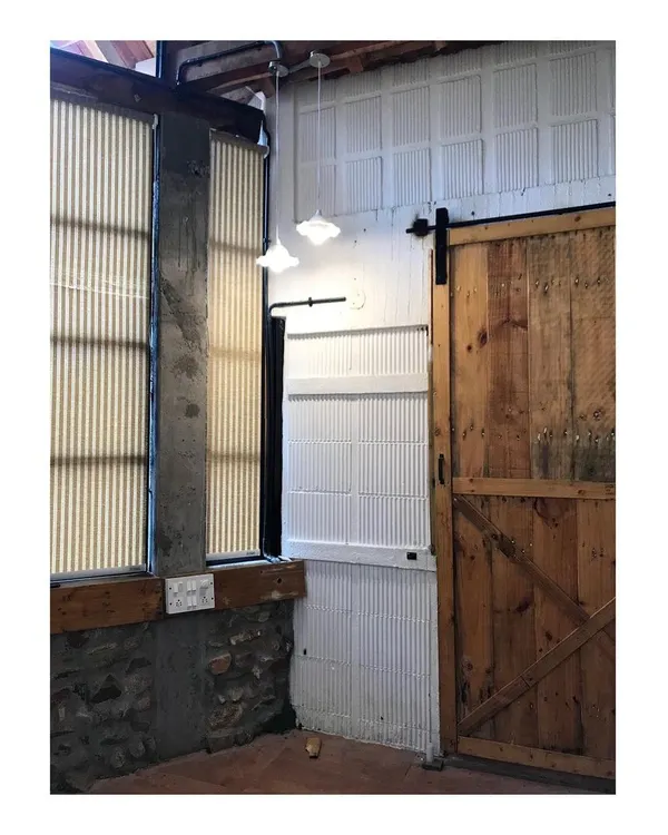 The entrance to the private farmhouse features a rustic wooden barn door and exposed stone and concrete walls. These locally sourced, natural materials set the tone for the sustainable and earthy architecture of the home.