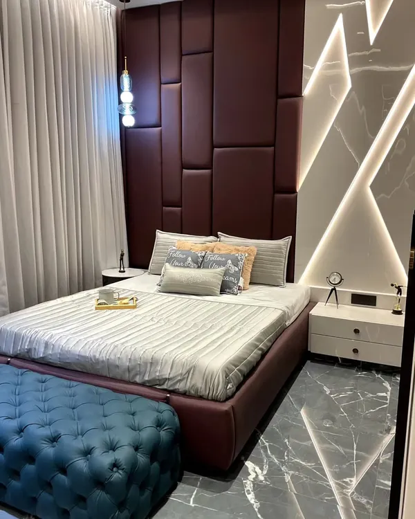 This bedroom showcases a full-height, geometric headboard in a deep burgundy upholstery, creating a bold focal point. The adjacent marble-effect wall panel features integrated LED backlighting, adding ambient light and a layer of modern luxury to the space.