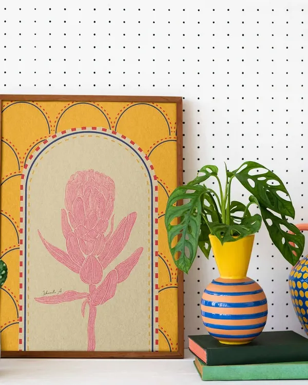 A framed print of a pink protea flower, set against a warm yellow, patterned background. This shows how my doodle style can be adapted into elegant botanical art for your home.