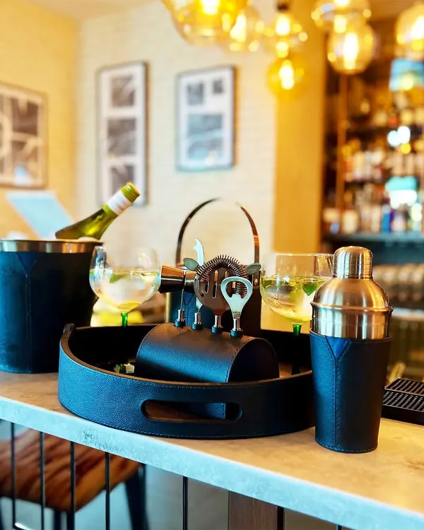 Elevate your home bar with the complete Bella Pelle Casa bar set. This image, set against a stylish bar backdrop, showcases the entire collection, including the tray, shaker, ice bucket, and toolset, all wrapped in sophisticated navy leather.