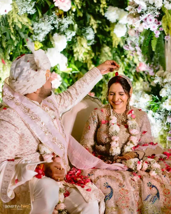 A groom gently places sindoor on his bride's forehead, a tender and significant moment during the wedding ceremony, surrounded by a cascade of flowers.