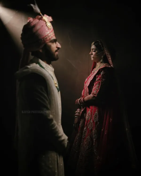 A powerful and artistic wedding portrait using a single spotlight to create a dramatic, cinematic feel. The image highlights the bride and groom's profiles as they face each other.