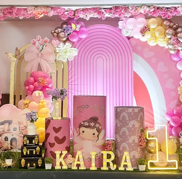 This enchanted forest theme for a first birthday is a perfect example of how I transform a space into a magical wonderland. The setup includes a custom backdrop, themed plinths, marquee lights for the name 'KAIRA', and a lush organic balloon garland.