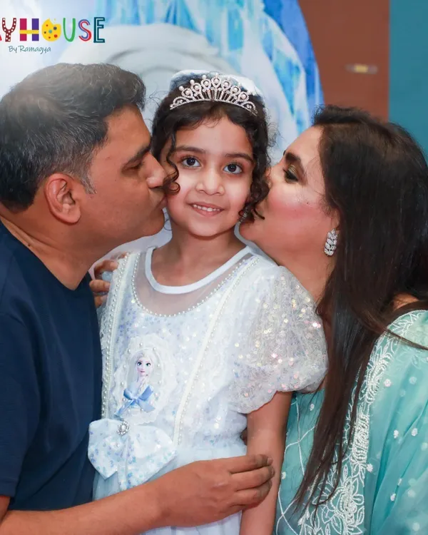 A beautiful moment of family love at Sofiya's Frozen-themed party. Dressed as a princess, she gets a kiss from her parents, capturing the magic of her special day.