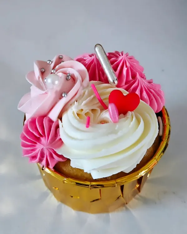 A close-up of my vanilla cupcake with two-toned strawberry and vanilla buttercream. It's decorated with silver sprinkles, a sugar pearl, and a little red heart for a lovely finish.