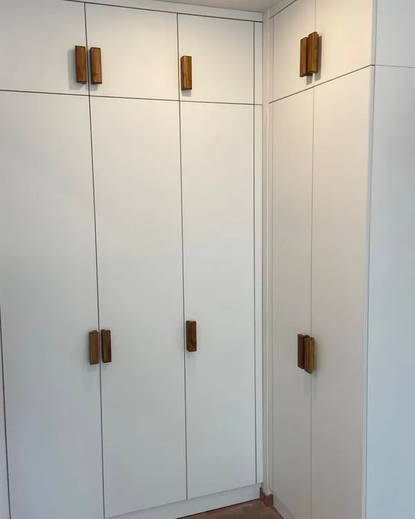 This Scandinavian-style wardrobe features custom-made handles in a natural wood veneer, providing a beautiful, warm contrast against the matte white shutters.