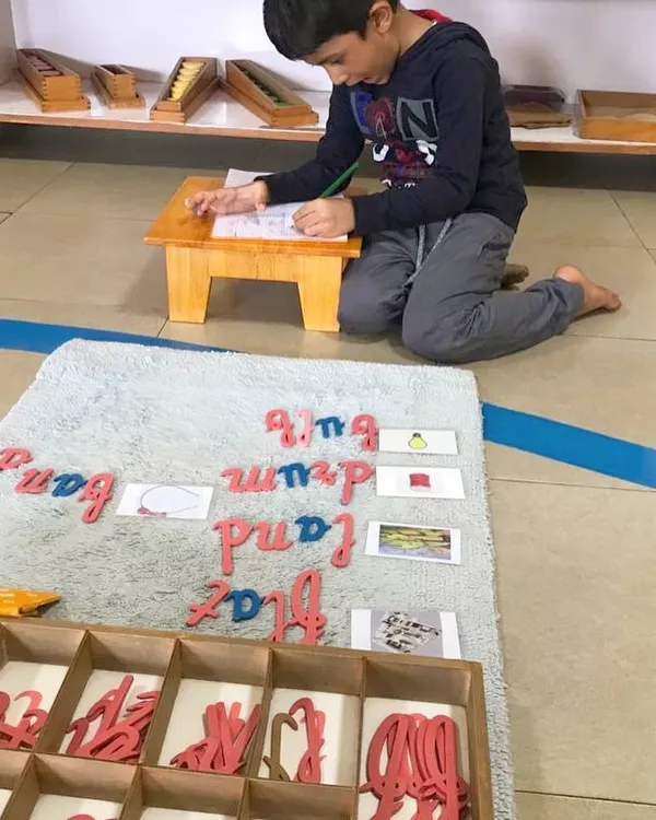 The Moveable Alphabet is where writing begins. Here, a child uses wooden cursive letters to build words, transforming his thoughts into written language before he has even mastered holding a pencil.