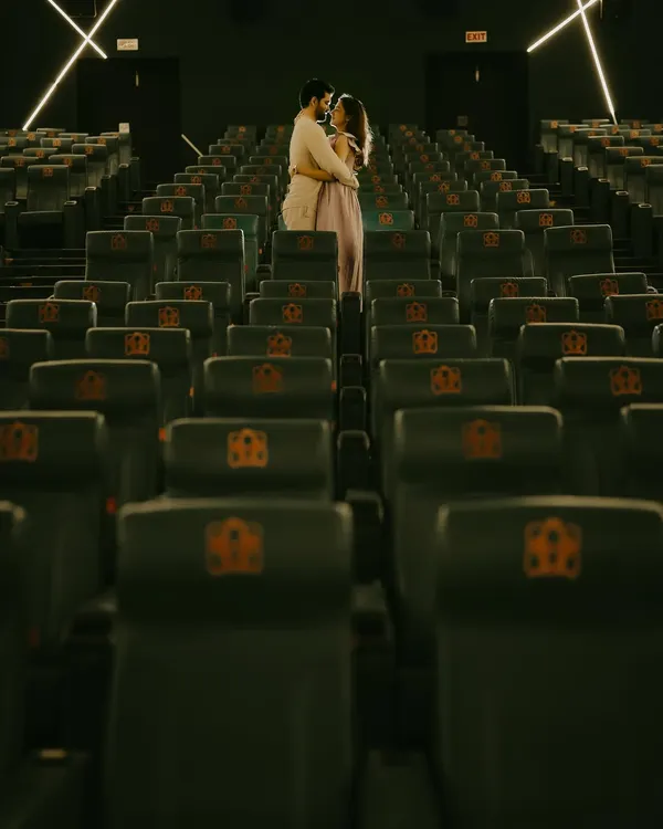 A wide shot of the couple embracing in an empty movie theatre. This unique pre-wedding shoot location turns their love story into its own feature film.