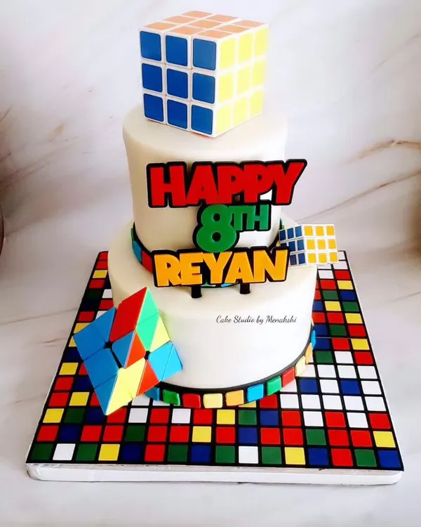 A stunning and complex Rubik's Cube themed cake. This two-tier cake sits on a board that looks like a scrambled cube, and features edible, handcrafted cubes on top.