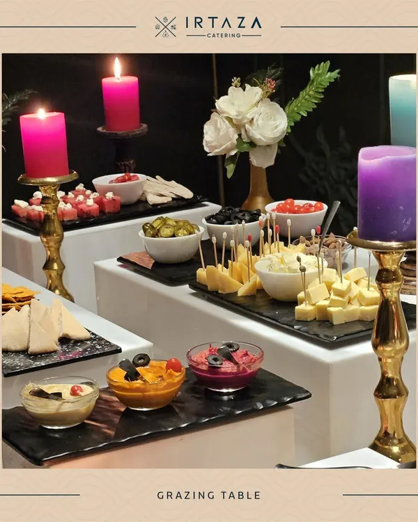 A lavish grazing table set up with an assortment of cheeses, dips, olives, and pita bread, all illuminated by colorful candles for a vibrant presentation.