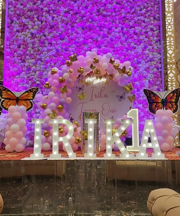 A grand butterfly-themed first birthday with a purple flower wall backdrop, large marquee letters, and butterfly cutouts.