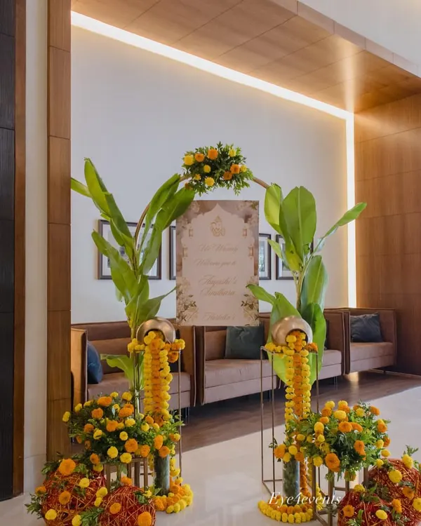 A warm and traditional welcome for guests. This entrance decor features bright yellow marigolds, lush banana leaves, and a personalized welcome sign, creating a festive and inviting atmosphere.