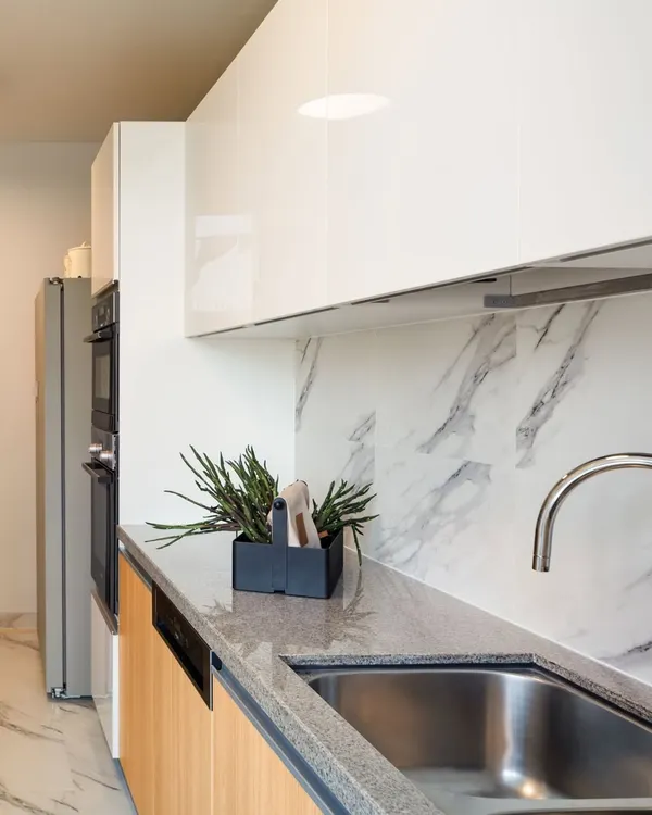A close-up of this modern kitchen reveals the material palette: glossy white upper cabinets, a durable granite countertop, and a marble-patterned backsplash. These choices balance beauty with resilience, ensuring the space is as practical as it is elegant.
