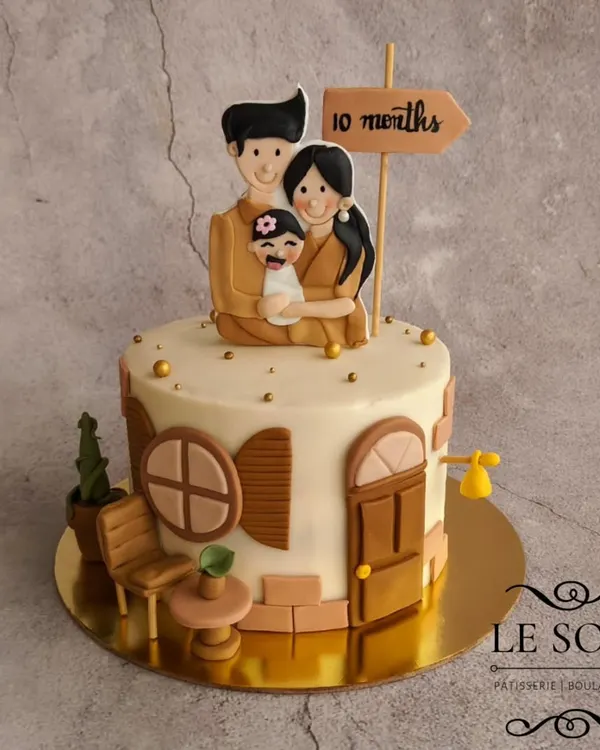 This cake celebrates a family's 10-month milestone with a "Home" theme. The half-kg Vanilla Butterscotch cake features a fondant family figurine on top of their house, with charming details like a tiny cactus and chair.