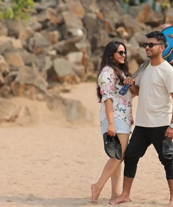 A relaxed and casual pre-wedding photo of a couple walking on the beach. The man carries a guitar, adding a personal touch to this candid moment of them enjoying a day out together.