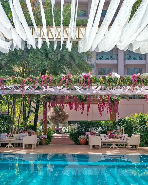 A 'Pomegranate Spring' themed Mehendi party by the pool. The design features elegant pergolas draped in sheer fabrics and bougainvillea, with comfortable lounge seating for a relaxed and celebratory atmosphere.