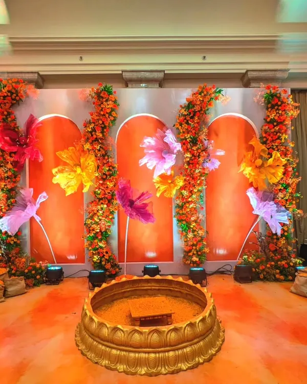 For this Haldi, I designed a unique stage with an orange backdrop and oversized, colorful paper flowers. The traditional brass urli in the center is ready for the ceremony, blending modern art with sacred ritual.