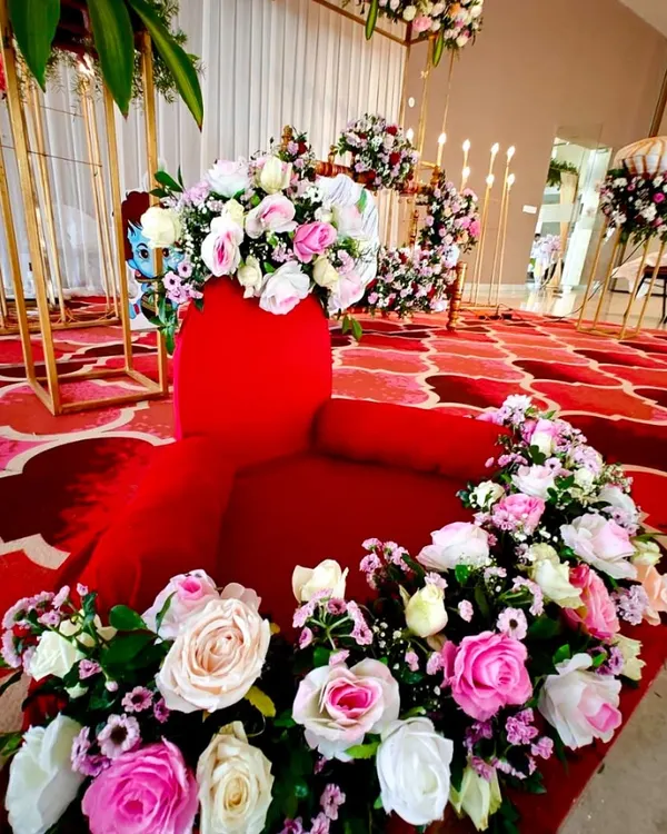 A beautiful setup for a naming ceremony, featuring a red velvet seat adorned with a garland of pink and white roses.