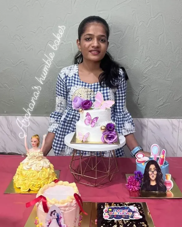 A happy student showcasing the variety of cakes made in a single workshop, including a doll cake, a tiered butterfly cake, and a photo print cake.